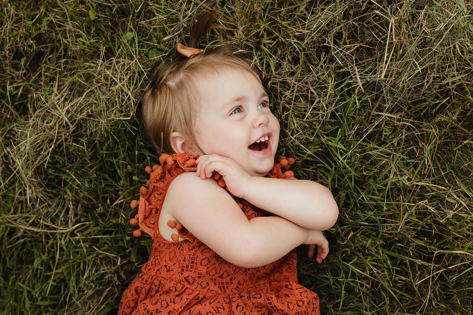 little girl in a rust color dress laughing while rolling in the grass City Sprouts St. Louis