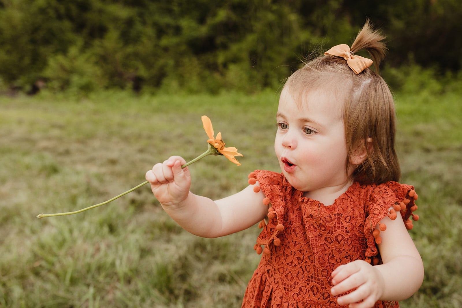 little girl in orange dress blowing on a flower Happy Up Inc