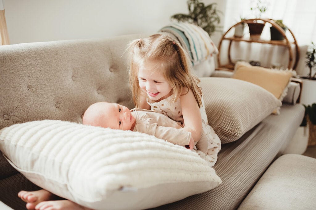 A big sister holds her newborn baby brother during a newborn photography session at home.