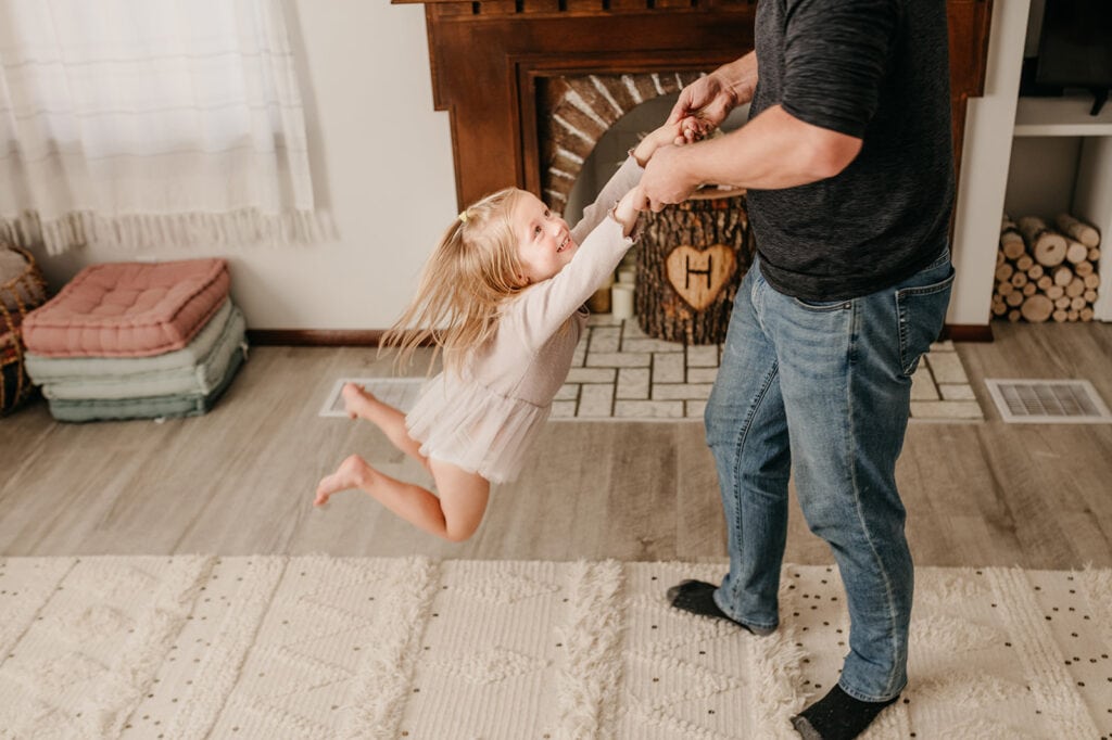 A dad playfully swings his daughter during their at home photography session