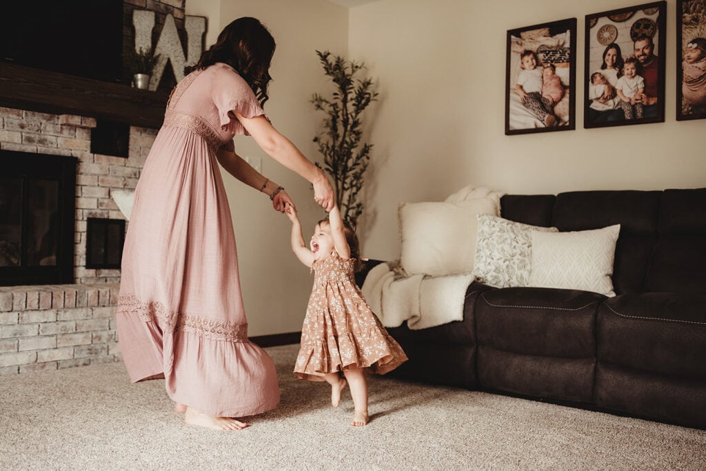 A mother and daughter dance around the living room for their at home photography session