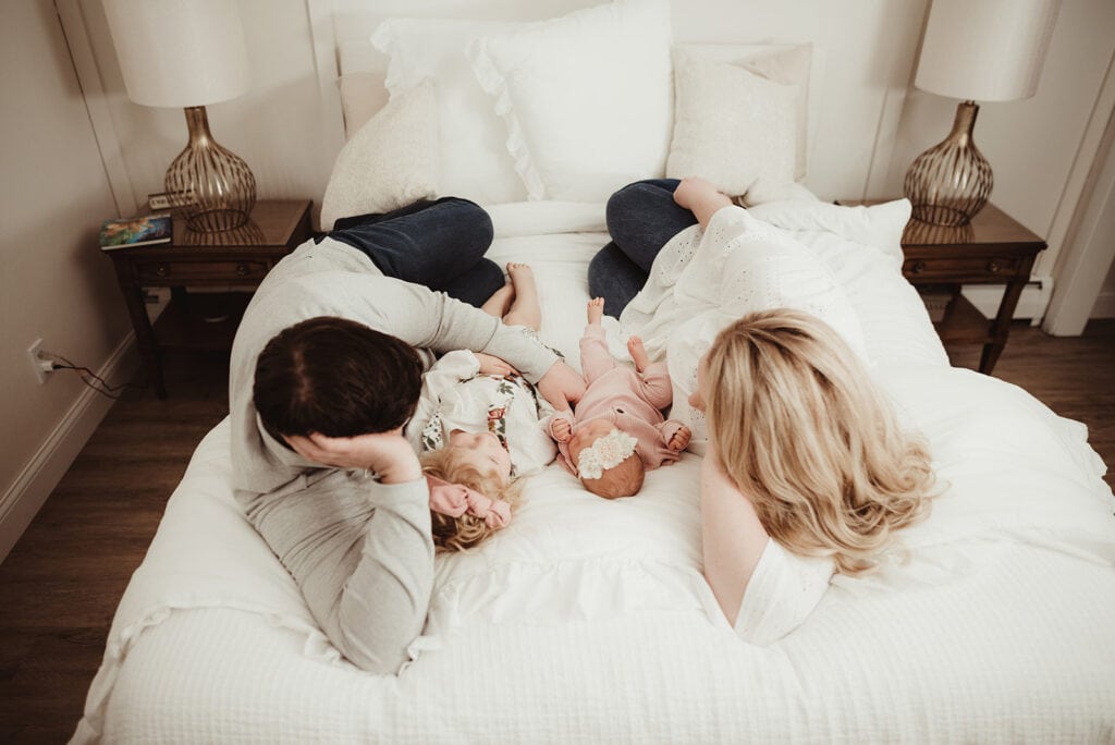 A family gathers around their newborn baby during a newborn photography session at home.