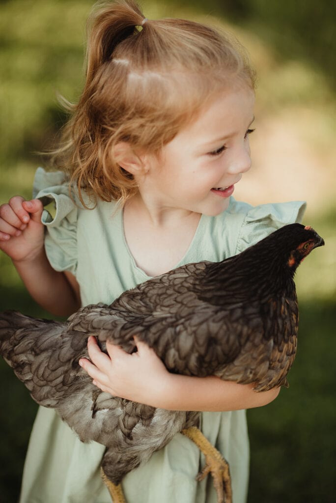 A child is holding a chicken during her in-home session.